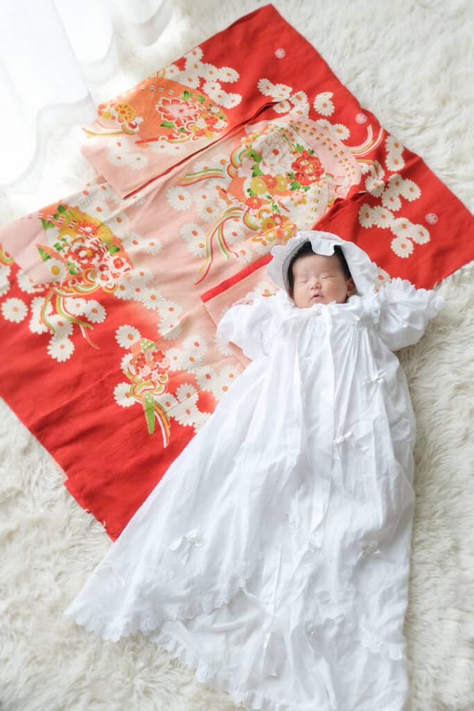 a baby in a white dress lying on a blanket