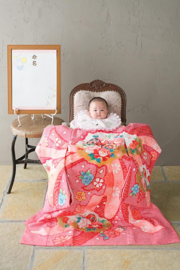 a baby sitting in a chair with a pink blanket